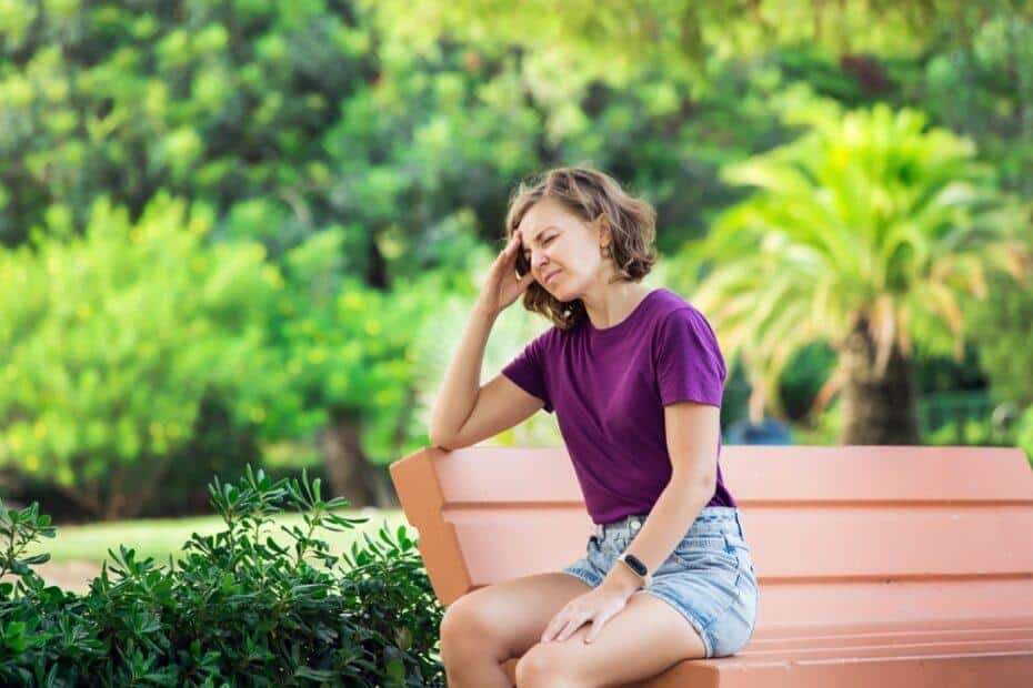 woman sitting outside holding her head in pain