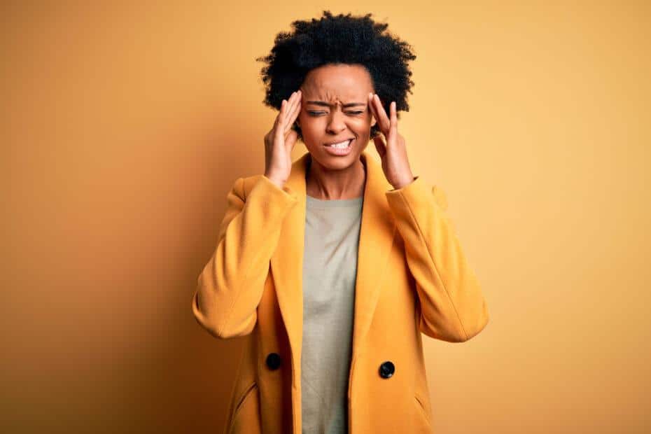 Woman in front of a yellow background holding her hands to her head.